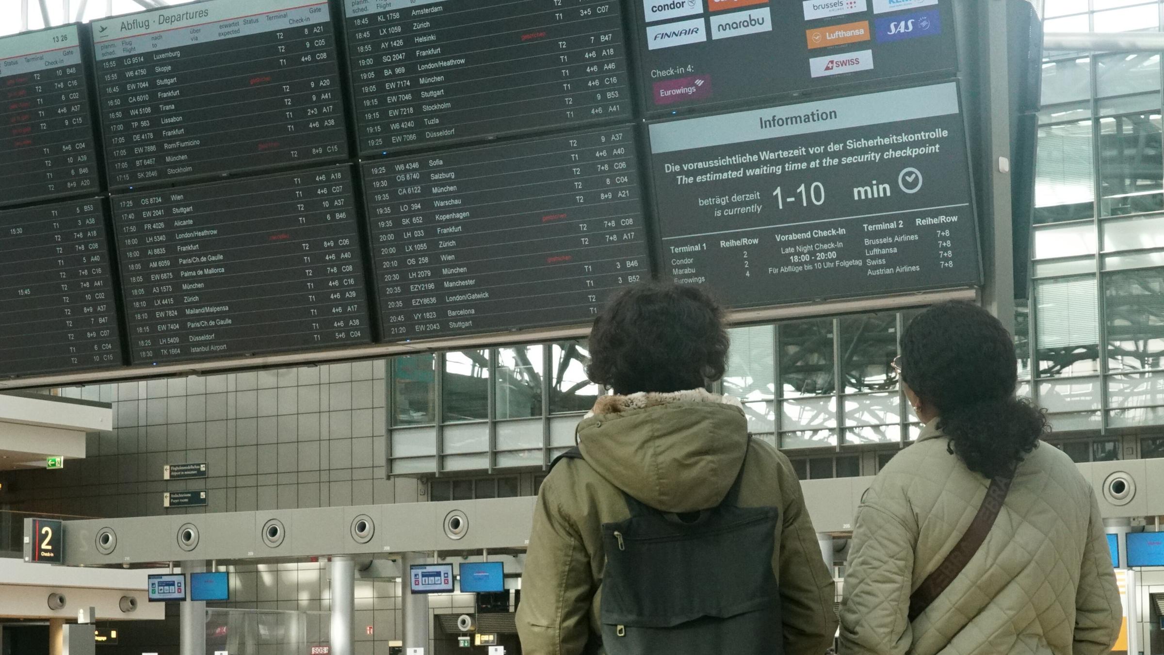 Reisende schauen am 12.03.2026 auf die Fluganzeige am Hamburger Flughafen.