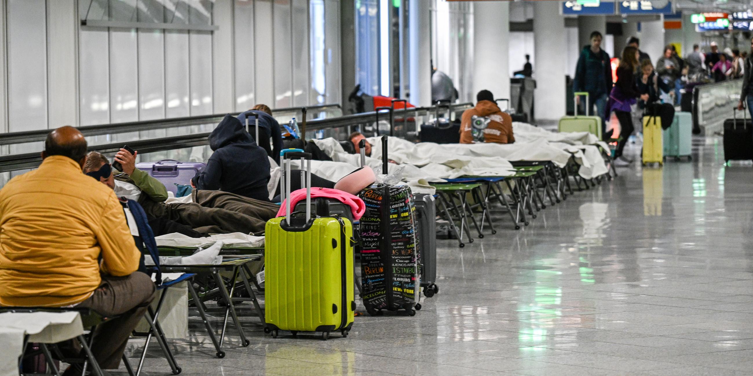 Menschen warten am Donnerstag Abend auf Feldbetten am Flughafen in München. Wegen Drohnensichtungen war der Flugbetrieb eingestellt worden. Zahlreiche Flüge fiehlen aus. 