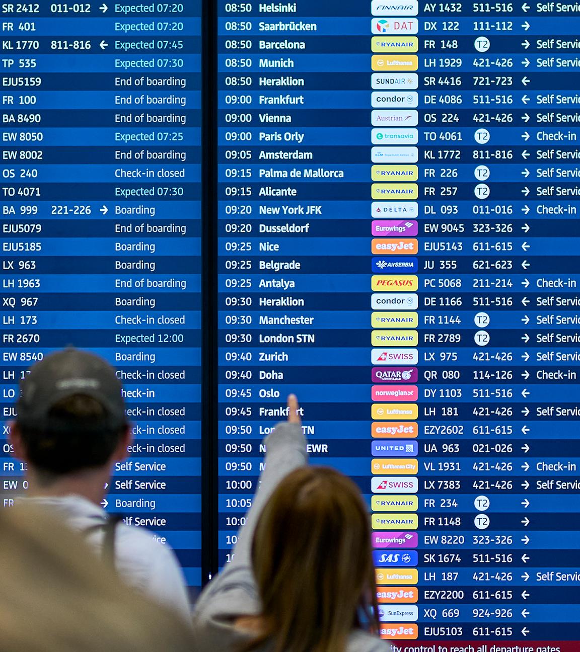 Menschen schauen auf die Abflugtafel am Flughafen