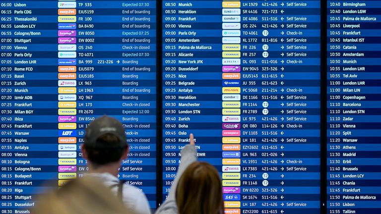 Menschen schauen auf die Abflugtafel am Flughafen