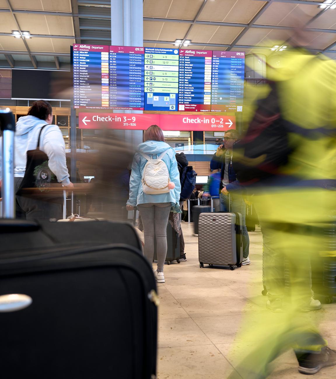 Flugreisende stehen vor der großen Anzeigetafel im Terminal 1 des Flughafens Berlin Brandenburg. 