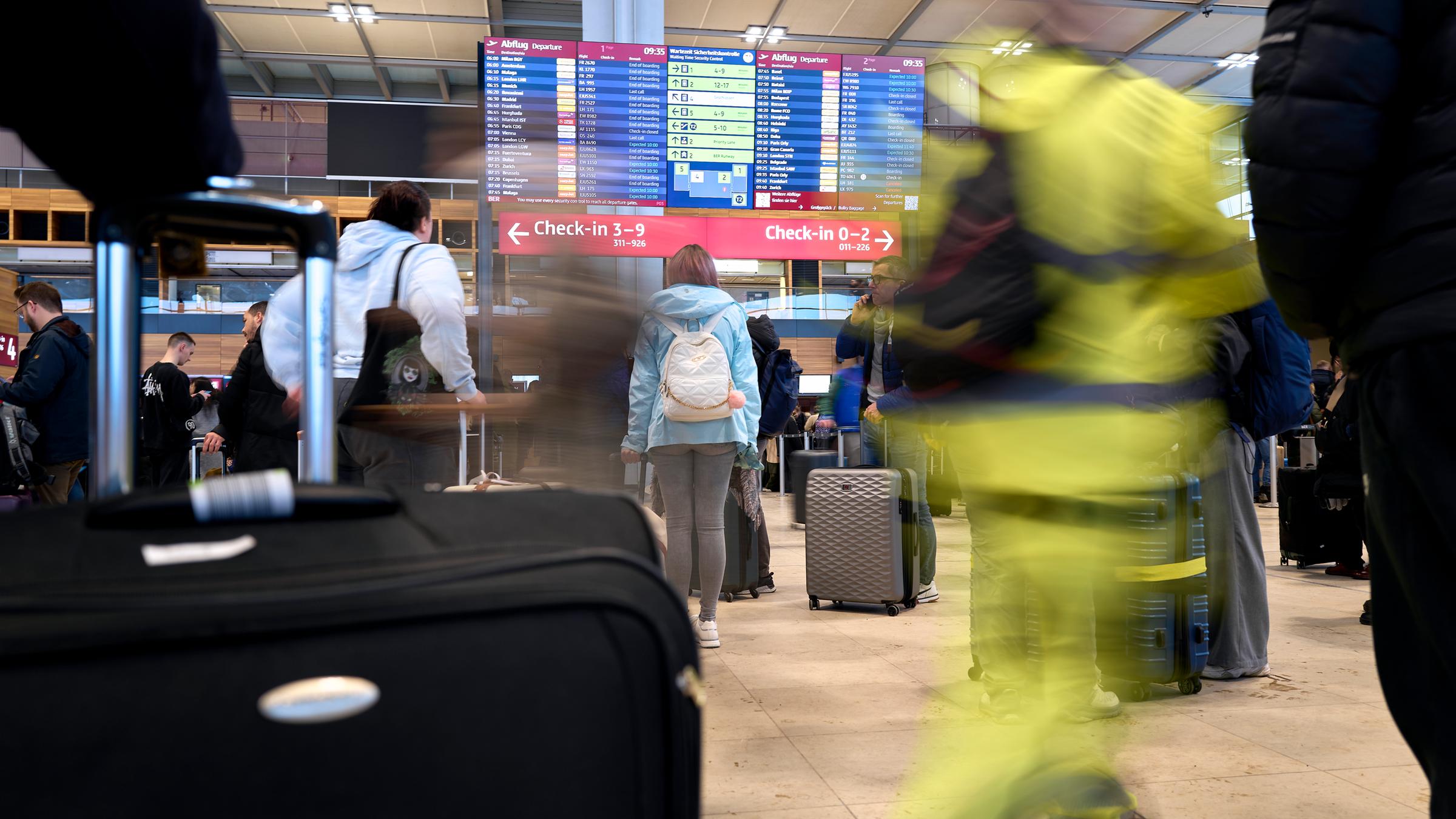 Flugreisende stehen vor der großen Anzeigetafel im Terminal 1 des Flughafens Berlin Brandenburg. 