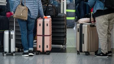 12.04.2025, Nordrhein-Westfalen, Landesweit: Fluggäste stehen in der Abflughalle im Flughafen Düsseldorf mit ihrem Gepäck vor den Schaltern.