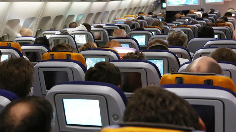 In einem Flugzeug sitzen Fluggäste auf ihren Plätzen.