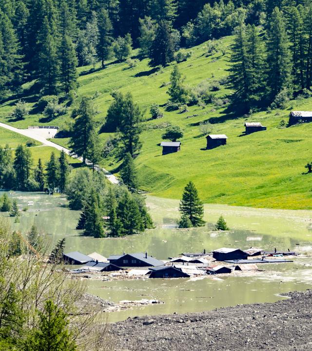 Schweiz, Blatten: Wasser aus dem Fluss Lonza fließt über Schlamm und Stein, nachdem sich ein See um den letzten Häusern des Dorfes Blatten gebildet hat. 