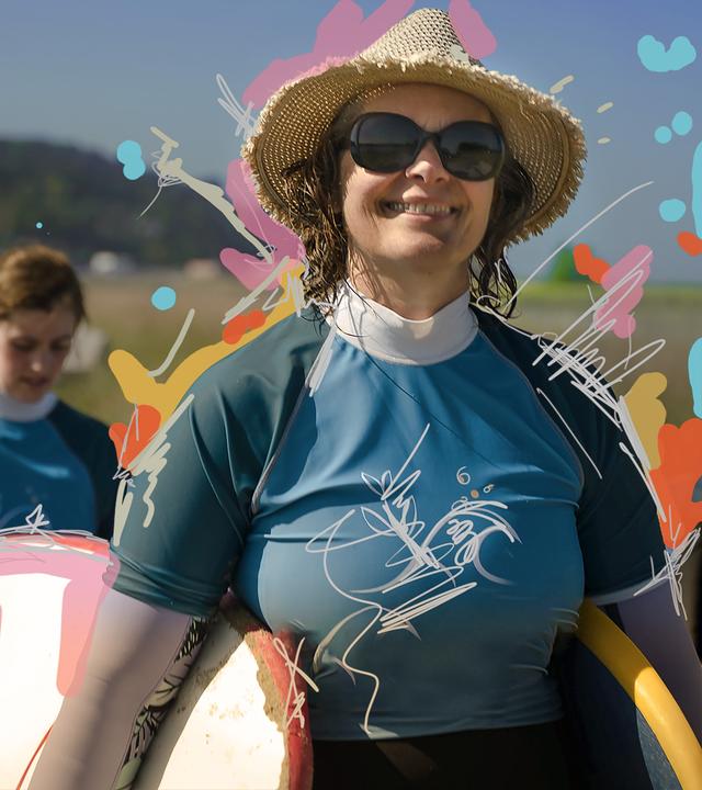 Eine Frau läuft lächelnd mit einem Surfbrett in der Hand auf die Kamera zu.
