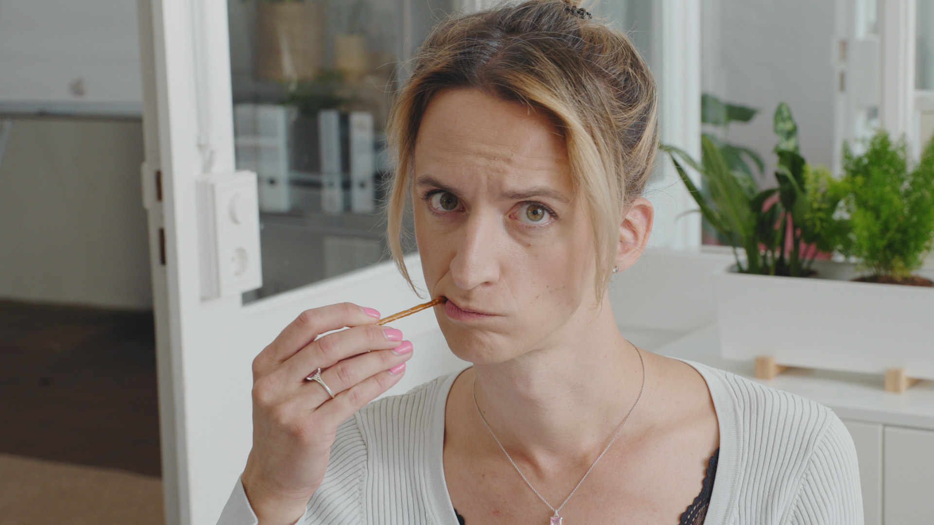 Eine Frau isst eine Salzstange. Sie hält die Salzstange in der rechten Hand. Sie trägt ein weißes Oberteil.