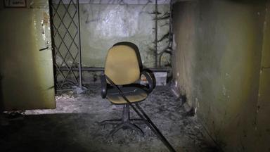 Stuhl, auf dem eine Eisenstange liegt, steht in dreckigem Kellerraum.