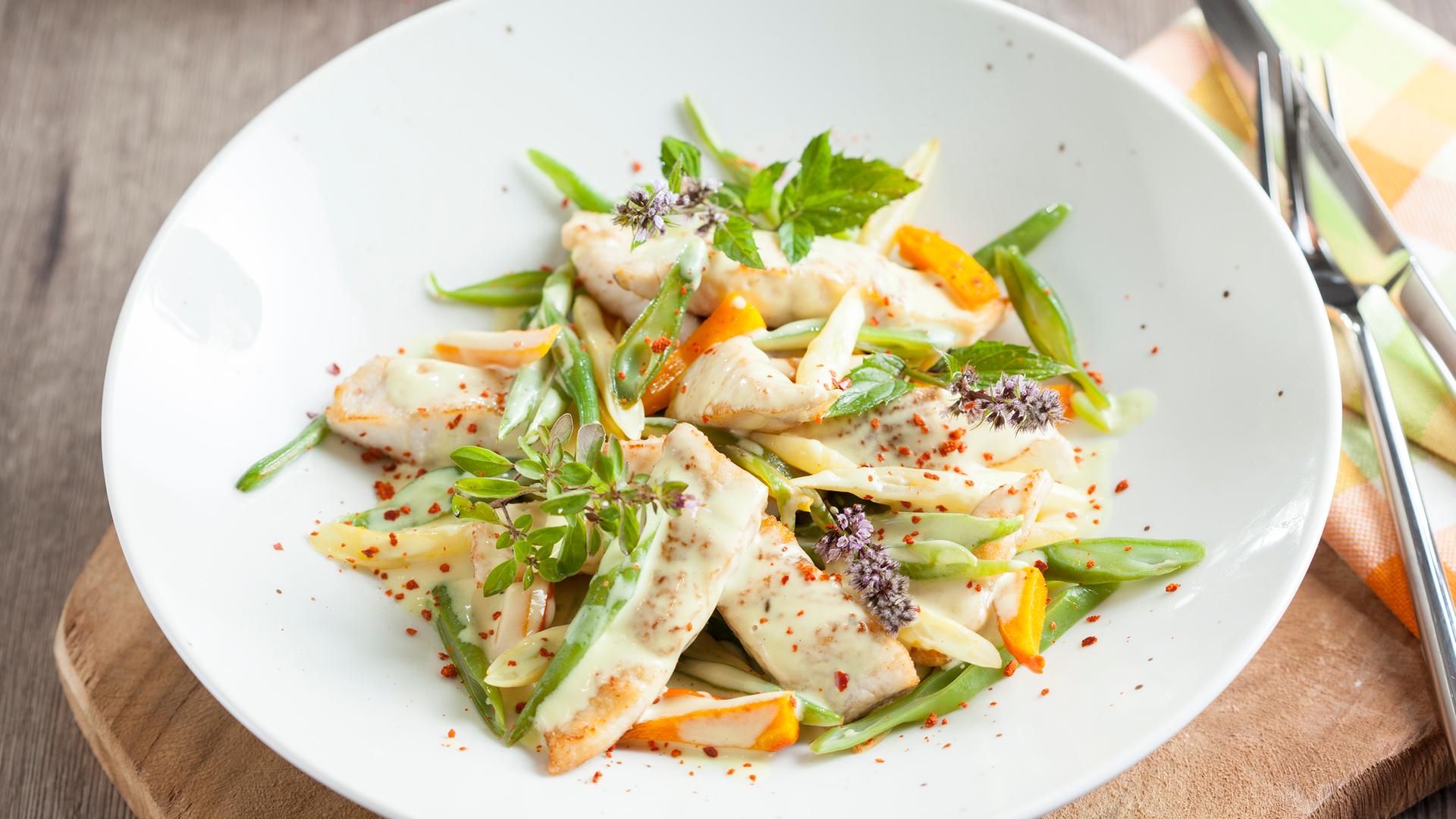 Forellengeschnetzeltes mit Sommerbohnen und Möhren in einem tiefen Teller angerichtet.