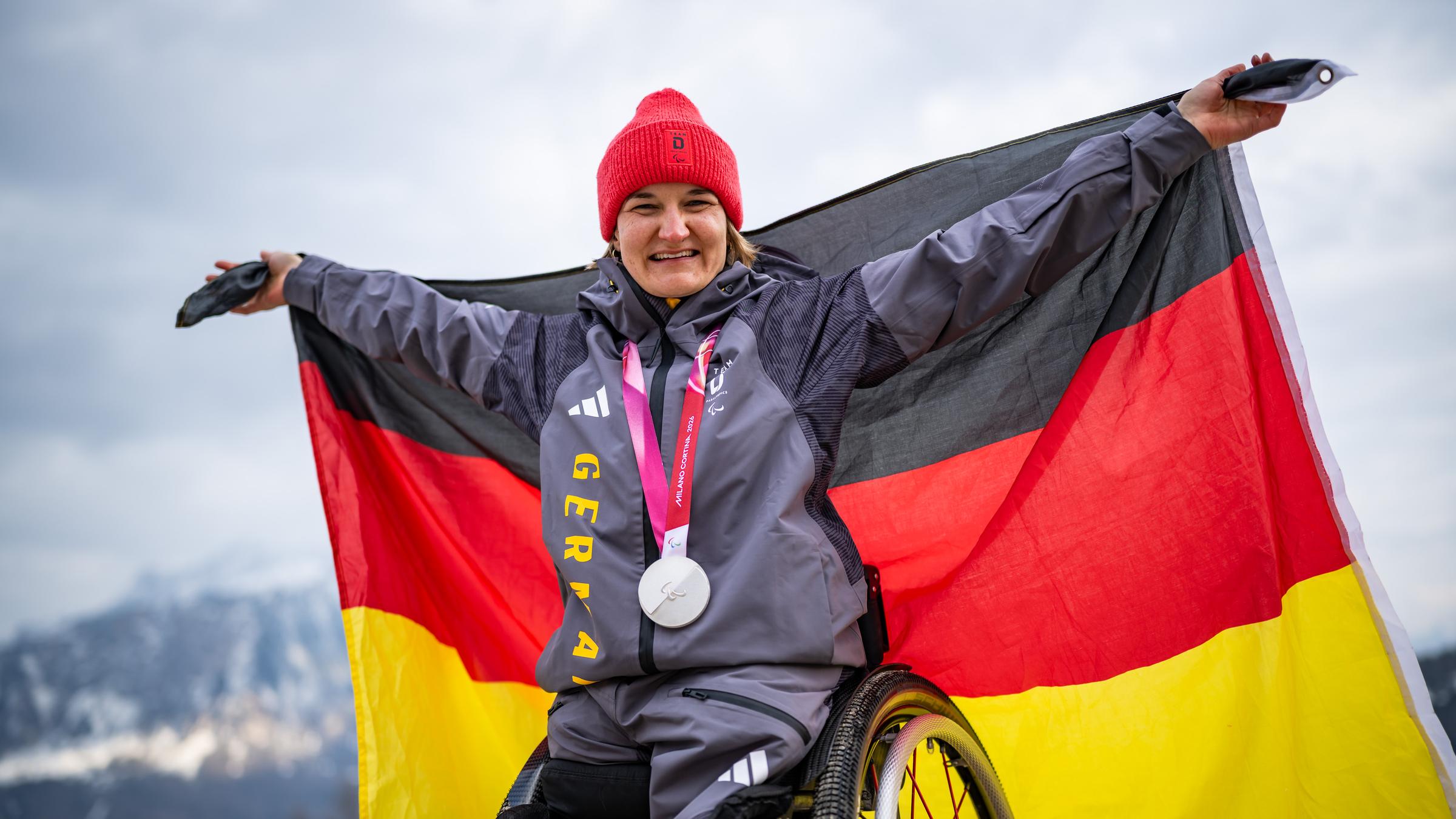 Anna-Lena forster streckt ihren Arm in die Höhe und feiert auf dem Podest ihre Silbermedaille.
