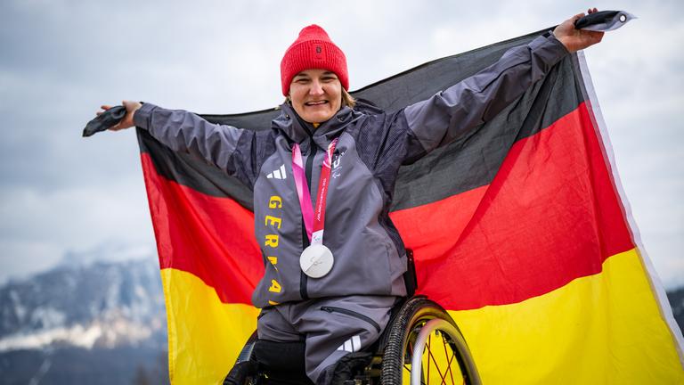 Anna-Lena forster streckt ihren Arm in die Höhe und feiert auf dem Podest ihre Silbermedaille.