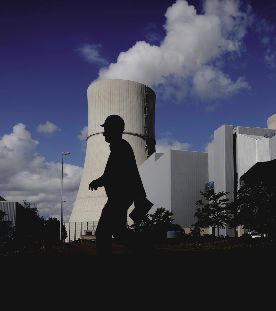 Eine Person mit Helm zeichnet sich ab als Silhouette vor dem angestrahlten Kuehlturm des Kohlekraftwerks Schwarze Pumpe in Spremberg, 04.08.2025.