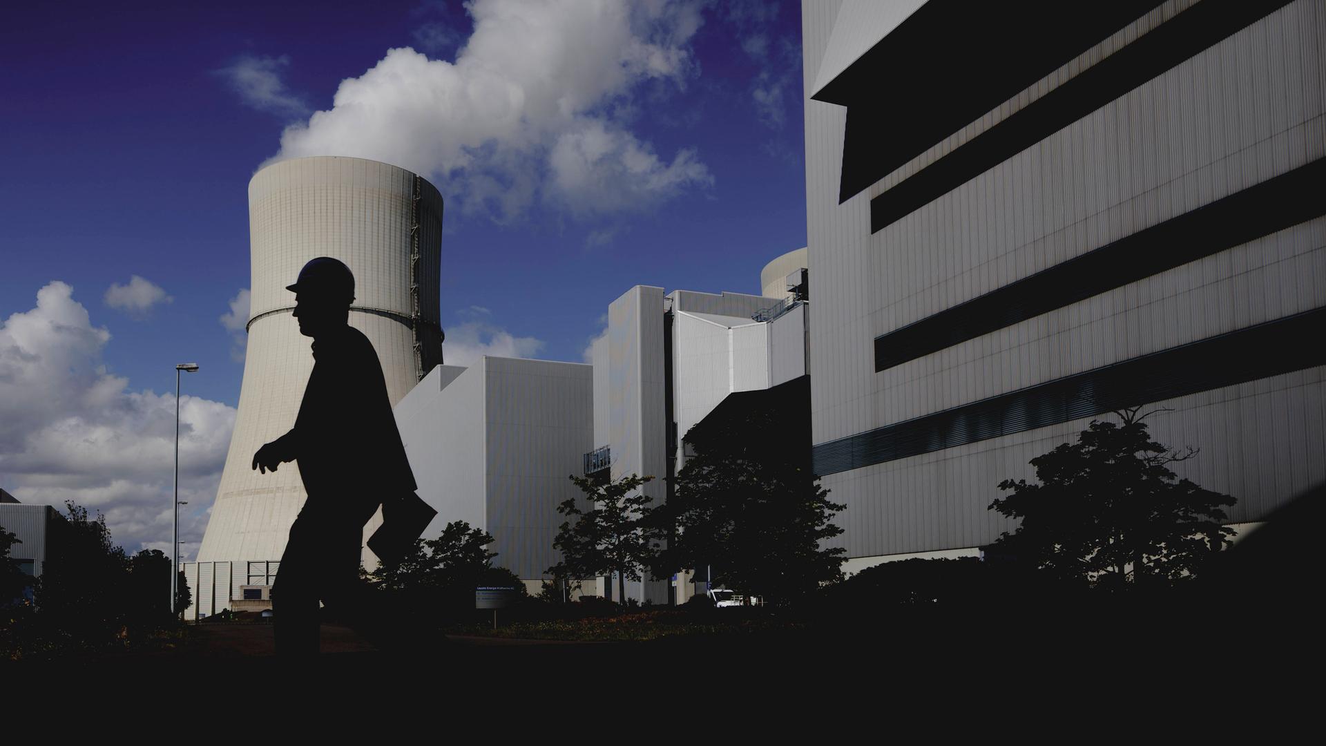Eine Person mit Helm zeichnet sich ab als Silhouette vor dem angestrahlten Kuehlturm des Kohlekraftwerks Schwarze Pumpe in Spremberg, 04.08.2025.