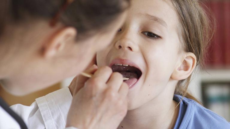 Kinderarzt guckt Mädchen in Mund