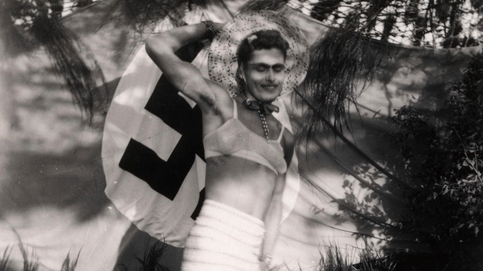 Ein Soldat aus der Wehrmacht während des Zweiten Weltkriegs posiert in erbeuteten Kleidern vor einer Hakenkreuzflagge.