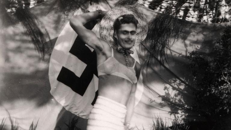 Ein Soldat aus der Wehrmacht während des Zweiten Weltkriegs posiert in erbeuteten Kleidern vor einer Hakenkreuzflagge.