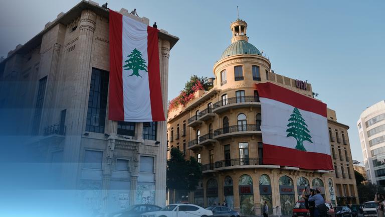 Zu sehen ist eine Straße und besonders zwei Gebäude mit großen libanesischen Flaggen, die einen Großteil der Gebäude-Fronten verdecken.