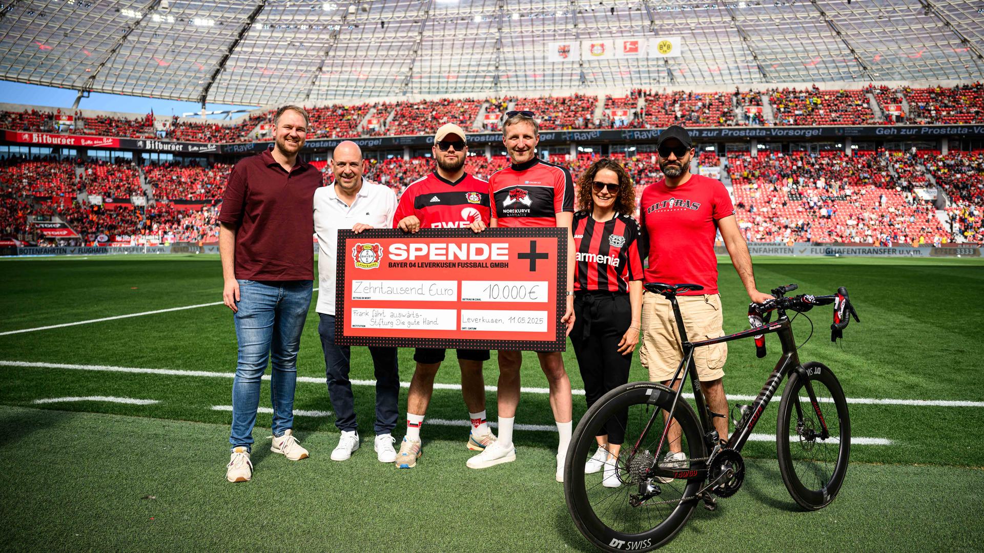 Frank Müller steht mit einem großen Spendenscheck im Stadion von Bayer Leverkusen