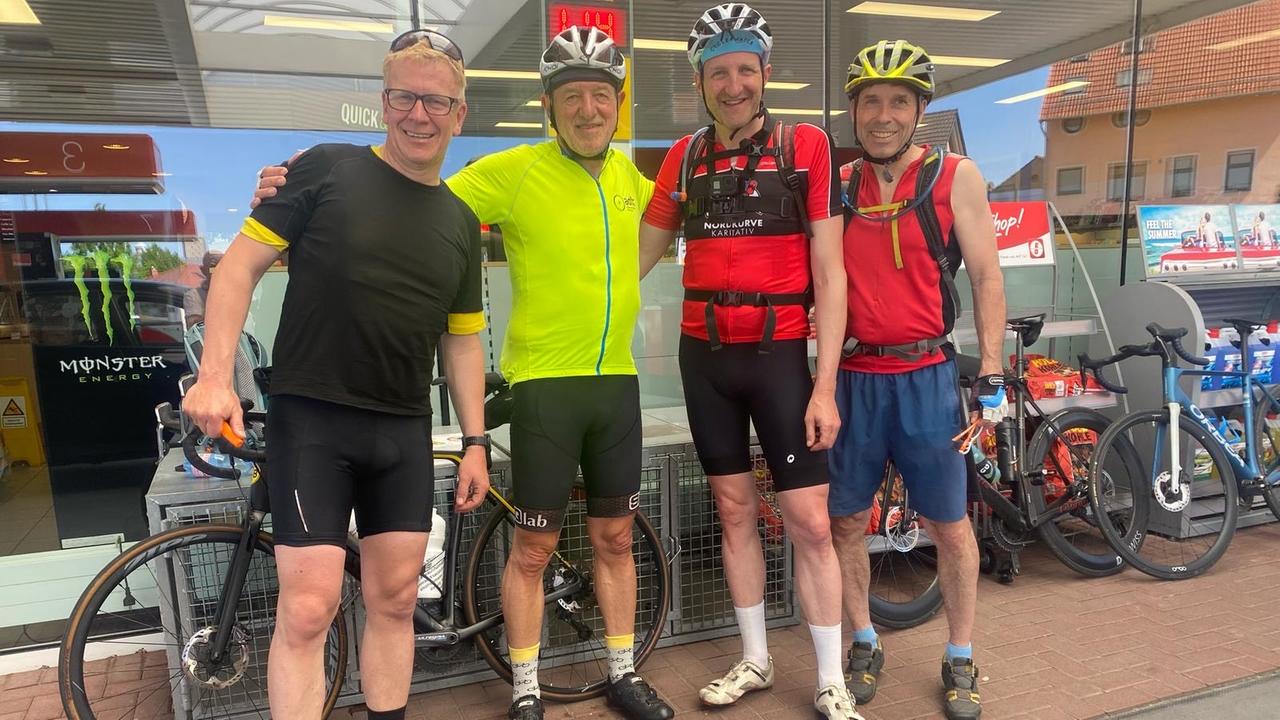 Frank Müller steht Arm in Arm mit seiner Fahrradgruppe vor einer Tankstelle