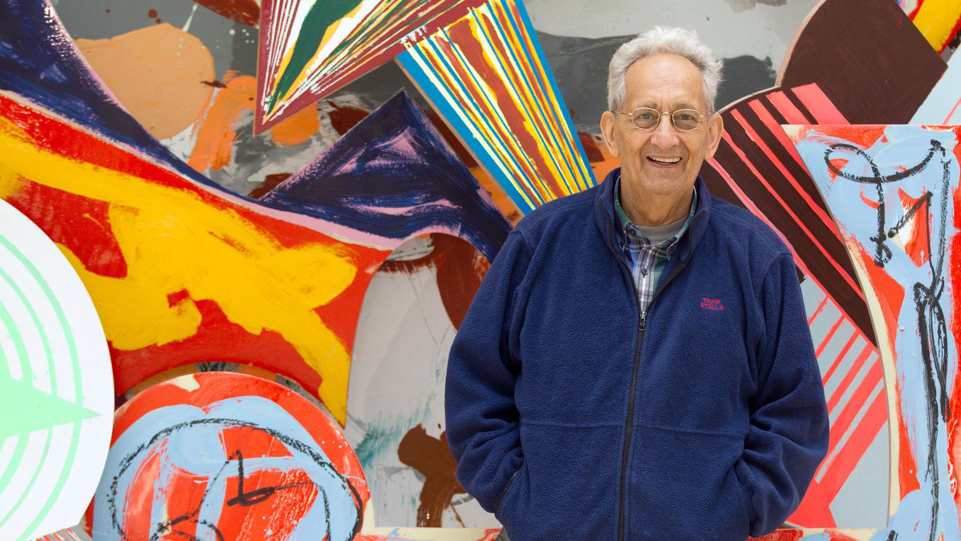 Frank Stella posiert vor einem farbenfrohen Werk im Kunstmuseum Wolfsburg