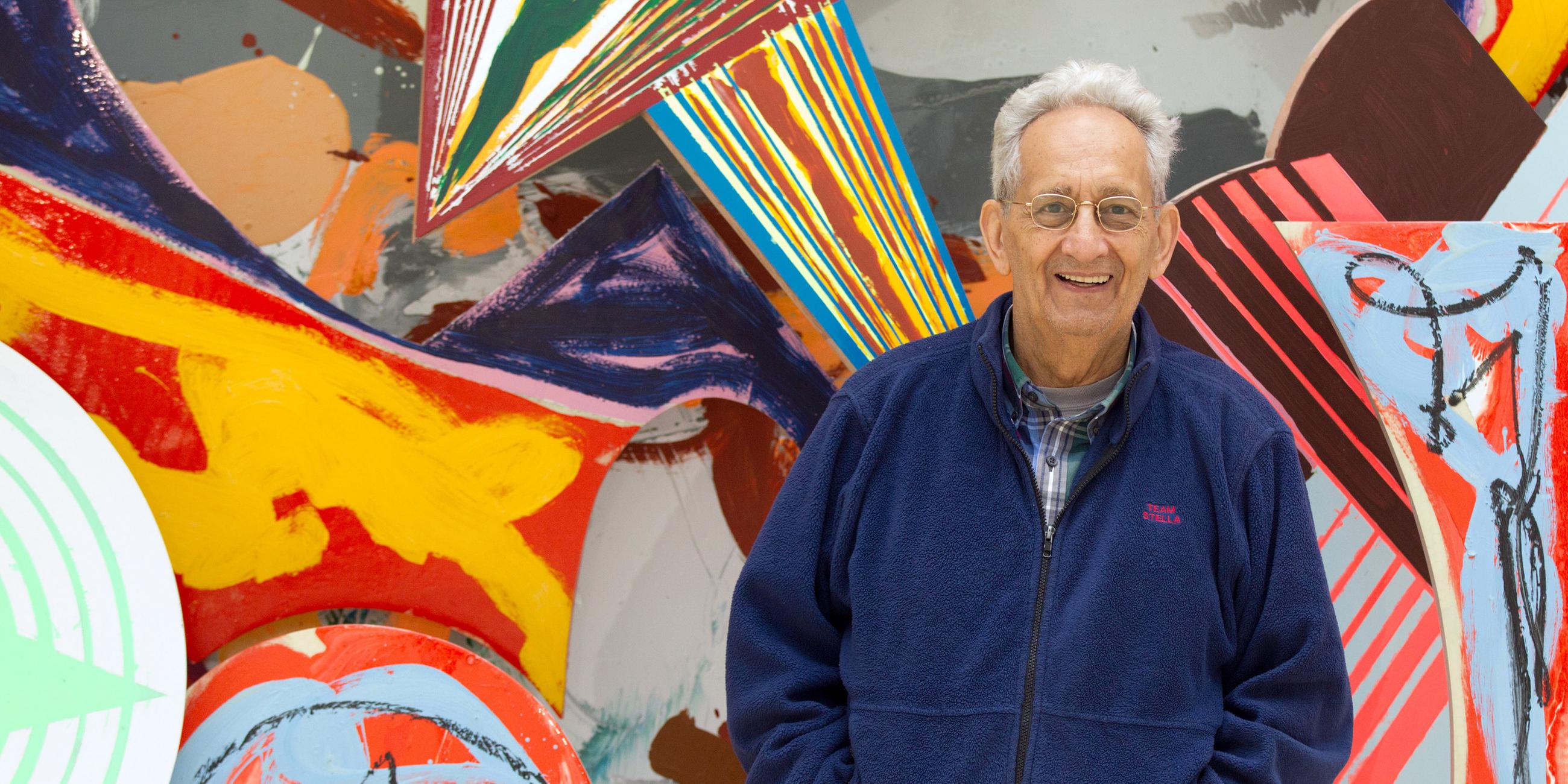 Frank Stella posiert vor einem farbenfrohen Werk im Kunstmuseum Wolfsburg