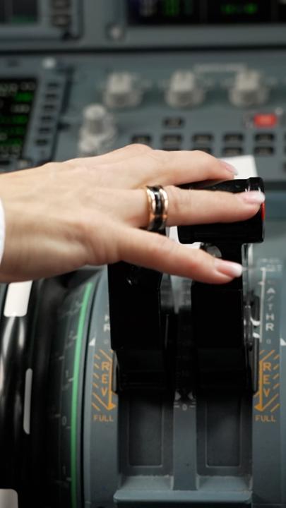 Die Hand einer Pilotin mit einem Ring am Ringfinger liegt auf einem Joystick im Cockpit eines Flugzeugs.
