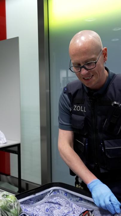 Nico Schneider (rechts), Zollmitarbeiter am Frankfurter Flughafen untersucht ein vor sich auf einem Tisch liegendes Gepäckstück eines Fluggastes auf verbotene oder zu versteuernde Substanzen.