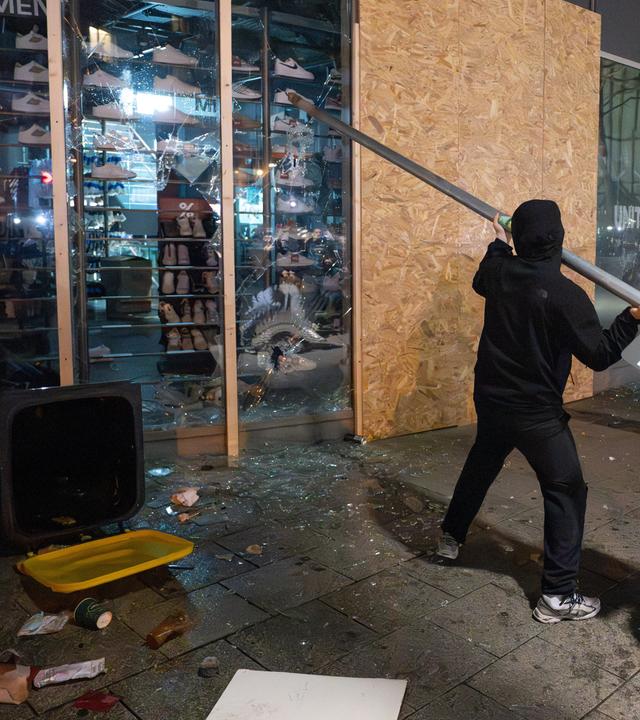 Ein Randalierer schlägt mit der Stange eines Straßenschildes auf ein Schaufenster eines Sneaker-Geschäfts ein.