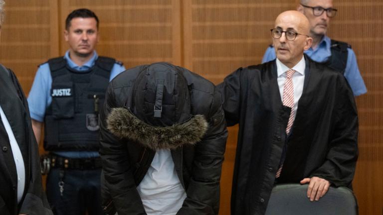 Der angeklagte, syrische Arzt (2.v.l.) steht vor der Urteilsverkündung neben seinem Anwalt Oussama Al-Agi (2.v.r.) im Oberlandesgericht. 