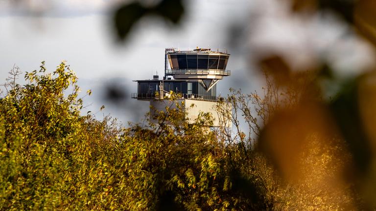 Symbolbild: Der Kontrollturm des Frankfurter Flughafens ist zwischen Blättern und dichter Vegetation zu sehen.