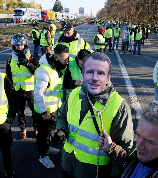 Demonstranten mit gelben Warnwesten laufen durch Frankreichs Straßen. Einer trägt eine Maske des französischen Präsidenten Macron am 17.11.2018 in Haulchin.