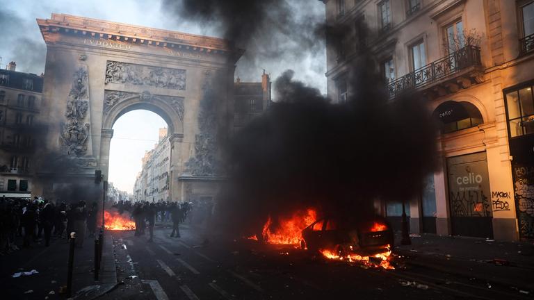 Demonstranten neben einem brennenden Auto in der Nähe der Porte Saint-Denis während einer Kundgebung gegen die „hohen Lebenshaltungskosten“ in Paris am 17. Oktober 2026 – im Rahmen eines landesweiten Mobilisierungsaufrufs, der verschiedene Gruppen vereint, die ihrem Unmut Ausdruck verleihen: ehemalige „Gelbwesten“, Schüler und Studierende, Klimaaktivisten sowie Landwirte.