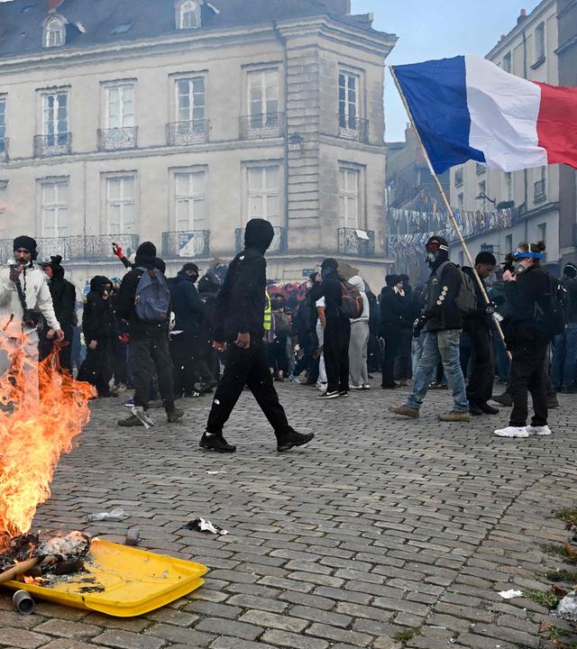 Ein Demonstrant schwenkt eine französische Flagge neben einem brennenden Mülleimer während einer Demonstration.