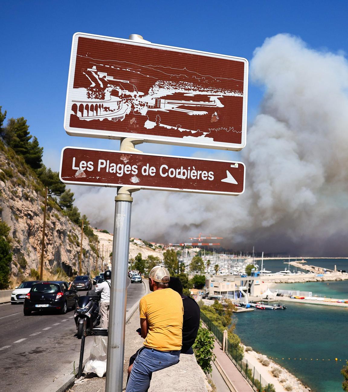 Menschen schauen zu in der Nähe von Marseille zu, während im Hintergrund der Rauch eines Waldbrandes wütet.