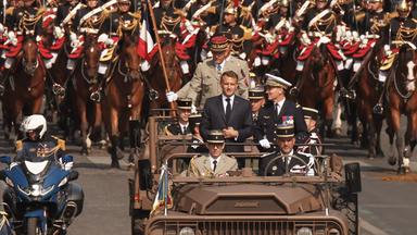 Der französische Präsident Macron steht zusammen mit dem Generalstabschef der französischen Streitkräfte, Mandon, im Kommandowagen während der Militärparade zum französischen Nationalfeiertag.