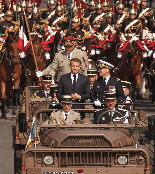 Der französische Präsident Macron steht zusammen mit dem Generalstabschef der französischen Streitkräfte, Mandon, im Kommandowagen während der Militärparade zum französischen Nationalfeiertag.