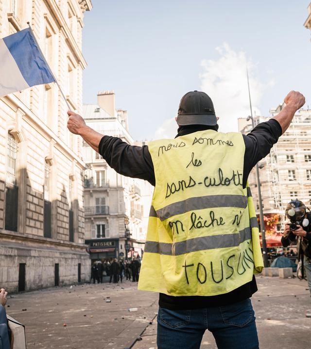 Frankreich, Paris: Ein Mann in einer gelben Weste hält eine französische Flagge während der Proteste gegen die steigenden Lebenshaltungskosten