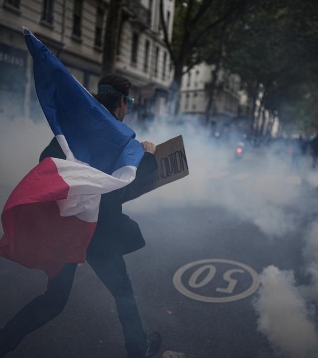 Ein Demonstrant hält eine französische Flagge in der Hand. Um ihn herum ist viel Rauch zu sehen.