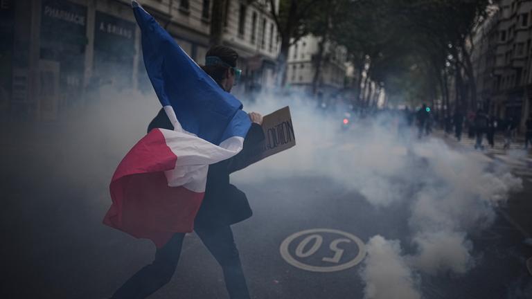 Ein Demonstrant hält eine französische Flagge in der Hand. Um ihn herum ist viel Rauch zu sehen.