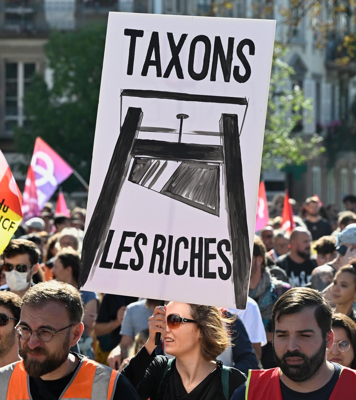 Frankreich, Straßburg: Demonstranten ziehen durch eine Straße. Eine Frau hält ein Plakat mit der Aufschrift "Taxons les Riches" in den Händen.