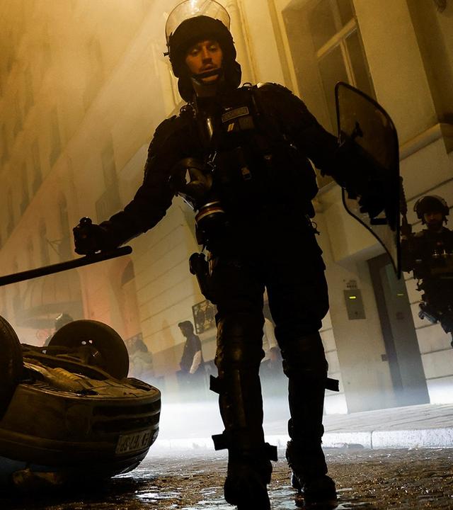 Ein Polizist steht nach gewaltsamen Protesten in Paris vor eine zersöten Auto. 