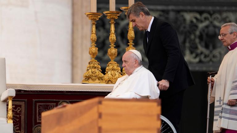 Papst Franziskus wird im Rollstuhl an dem Sarg des verstorbenen emeritierten Papstes Benedikt XVI. während öffentlichen Trauermesse für den emeritierten Papst Benedikt XVI. auf dem Petersplatz gefahren.