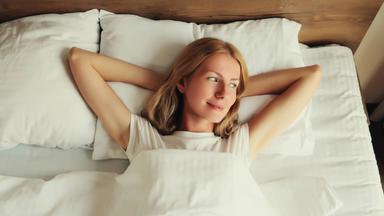 Junge Frau liegt nach dem Aufwachen noch lächelnd im Bett