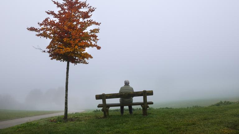 Baden-Württemberg, Uttenweiler: Eine Frau sitzt an einem Aussichtspunkt im Nebel auf einer Bank