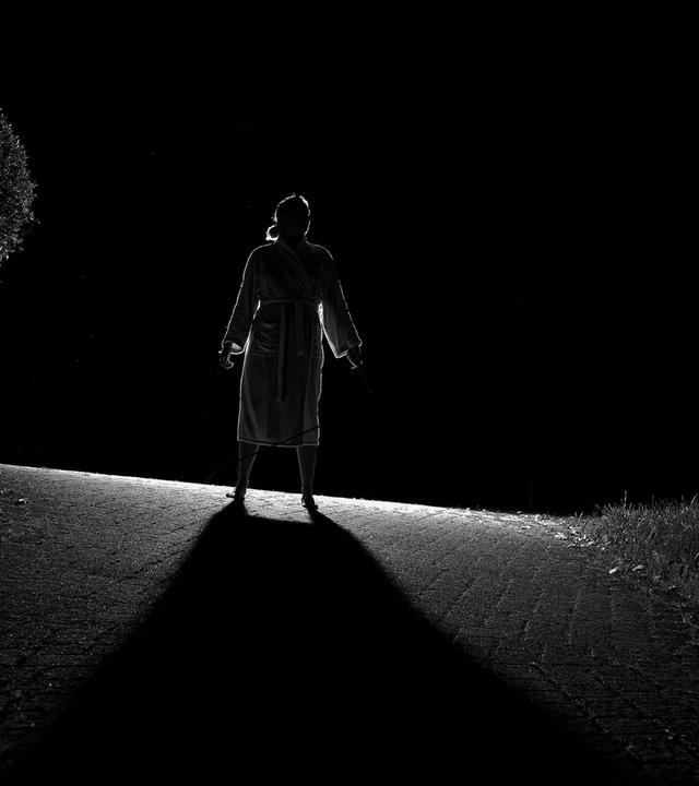 Eine Frau steht bei Nacht auf einer Anhöhe mit dem Rücken zum Betrachter und wird von vorne angeleuchtet, so dass sie als Schattenriss zu sehen ist.