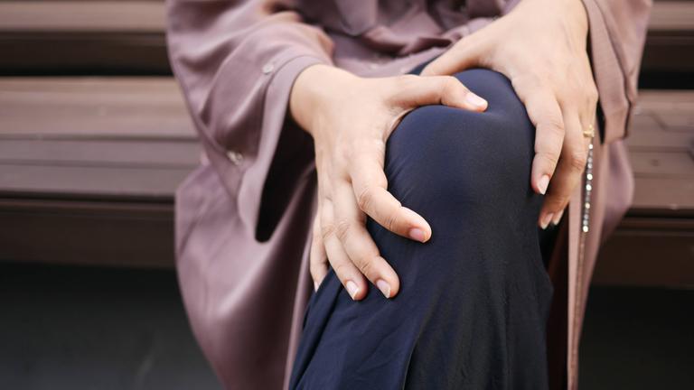 Nahaufnahme einer Frau, die auf einer Parkbank sitz und sich das Bein massiert.