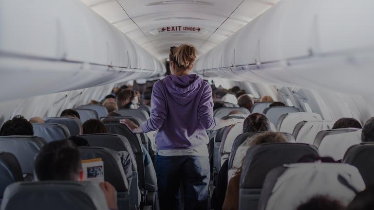 Der Innenraum eines Flugzeugs mit Passagieren auf den Sitzen und einer Reisenden, die durch den Gang geht.
