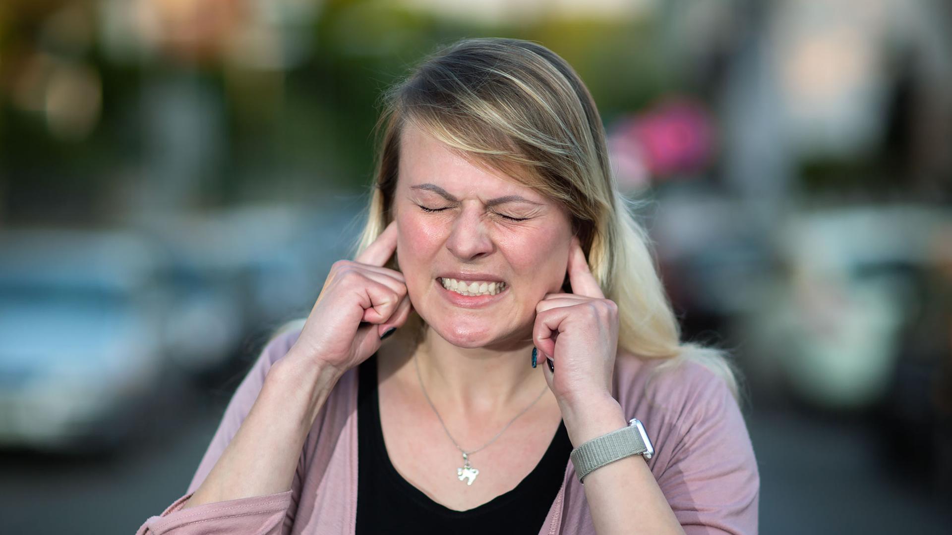 Frau hält sich die Ohren zu