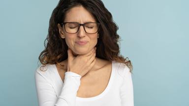 Frau fasst sich mit einer Hand an den Hals und verzieht das Gesicht