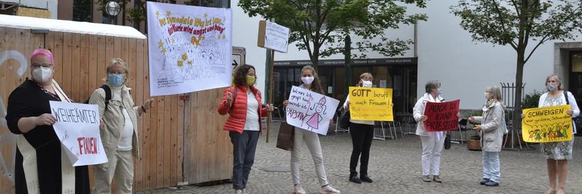 Eine Gruppe von Frauen steht auf einem Platz und hält ihre bunten Protestschilder in den Händen.
